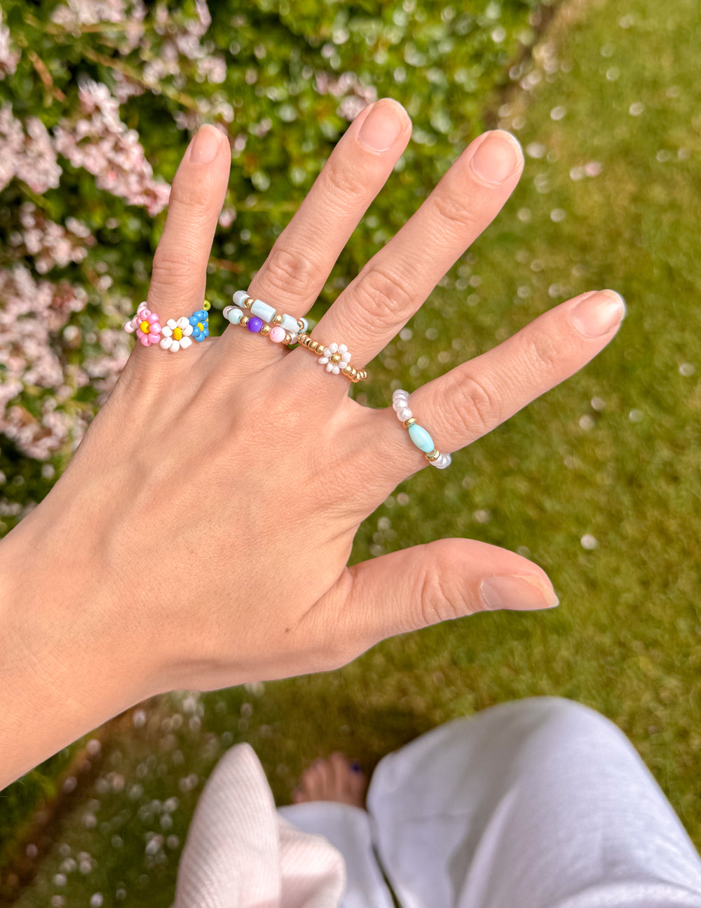 Pastel beaded rings on hand with blue, pink, purple and white daisy bead details