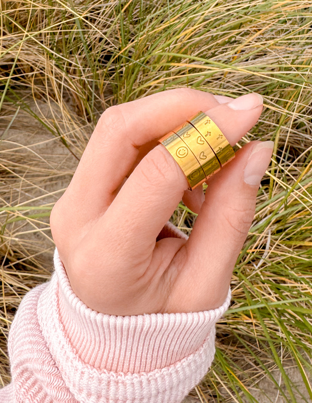 Gold-tone engraved ring set on hand, two slim stacked bands with engraved icon patterns