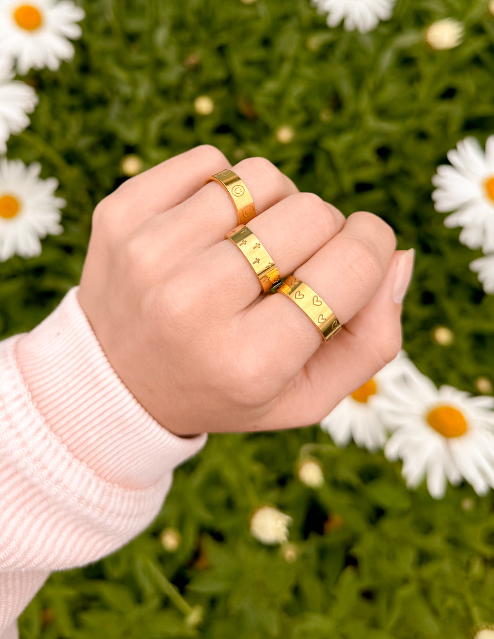 Gold-tone engraved ring set on hand: two slim bands with smiley and heart symbols