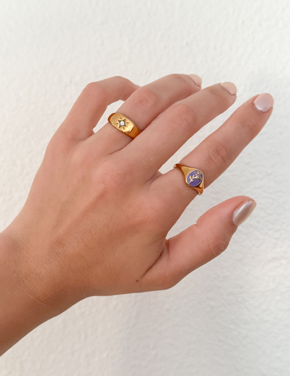 Gold signet rings with blue and yellow enamel starburst motifs and gemstones on hand