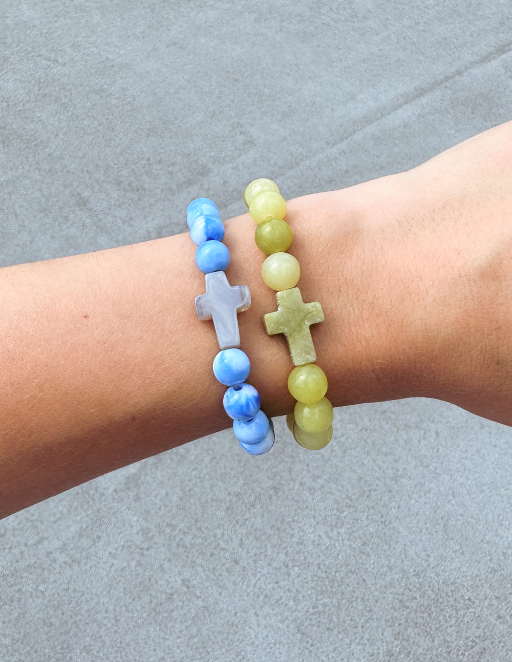 Blue and light green beaded bracelets with cross charms on wrist