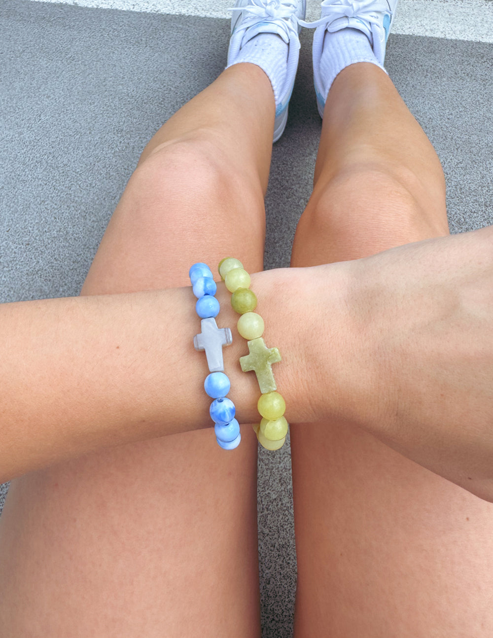 Two beaded cross bracelets, blue and light green, on crossed wrists