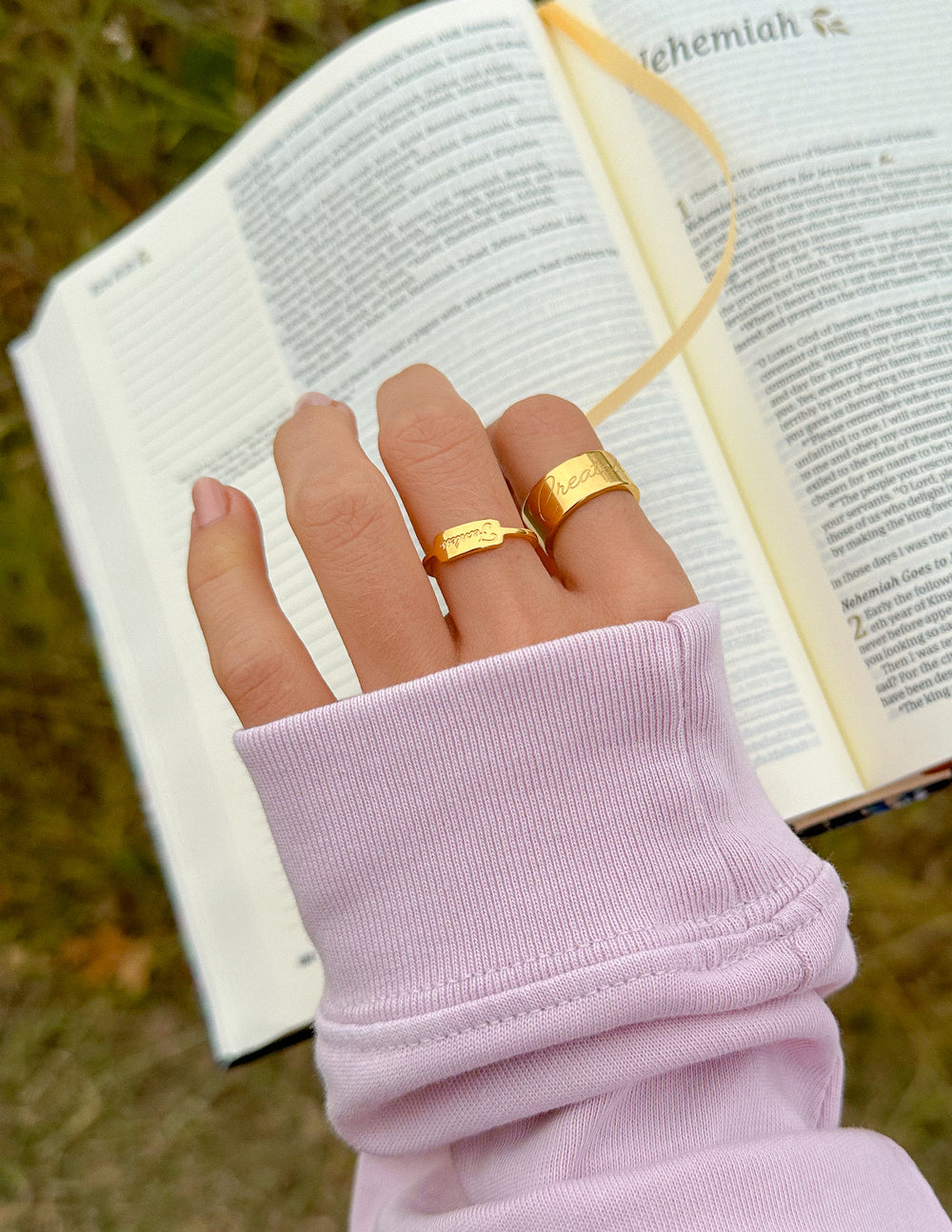 Gold band ring with engraved face on hand holding an open book