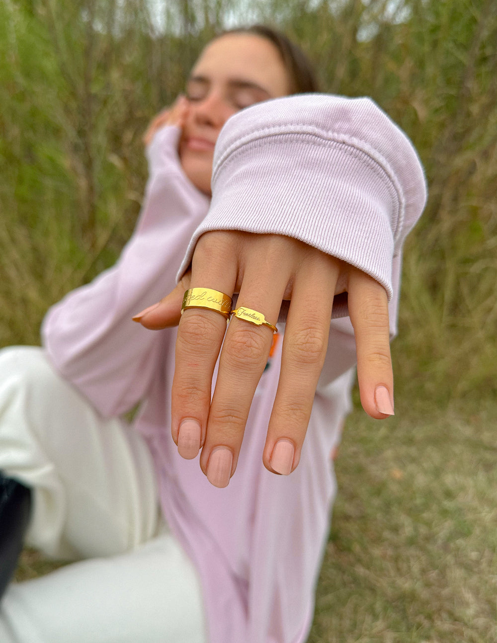 Gold engraved band ring on hand over lavender hoodie, outdoors