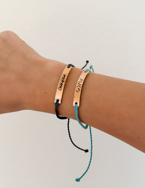 Tan leather bracelet with blue cord and black cord, engraved metal bar and charms