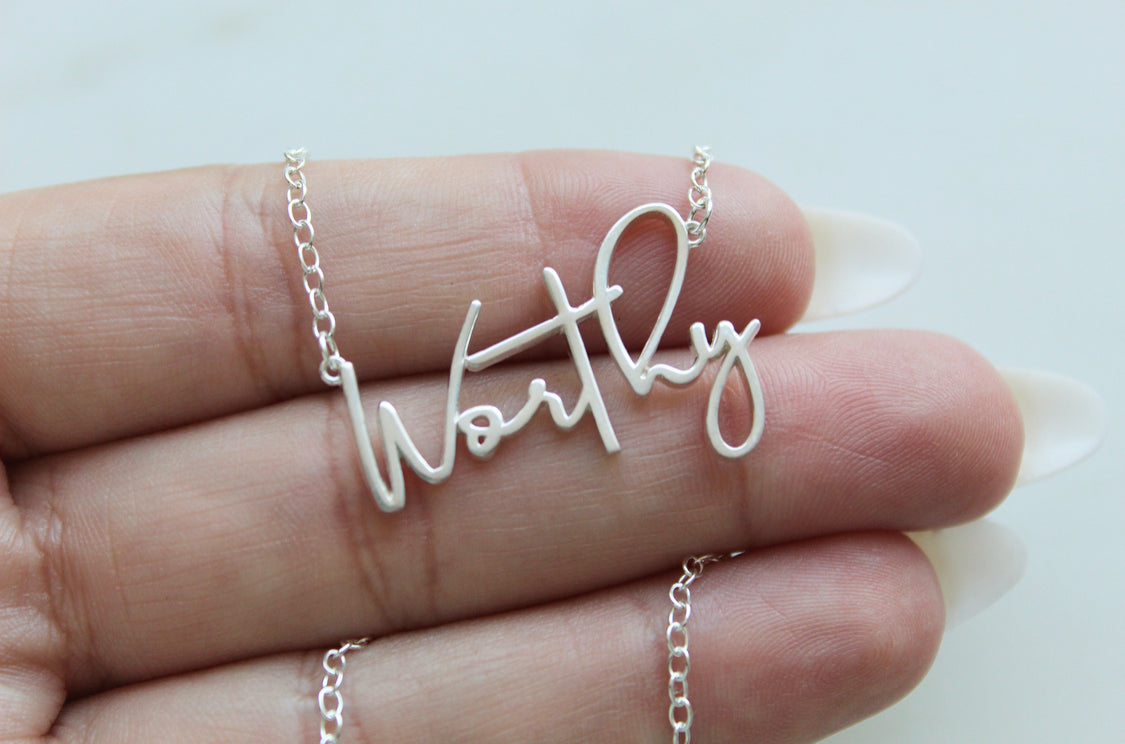 Sterling silver Worthy pendant necklace held in hand