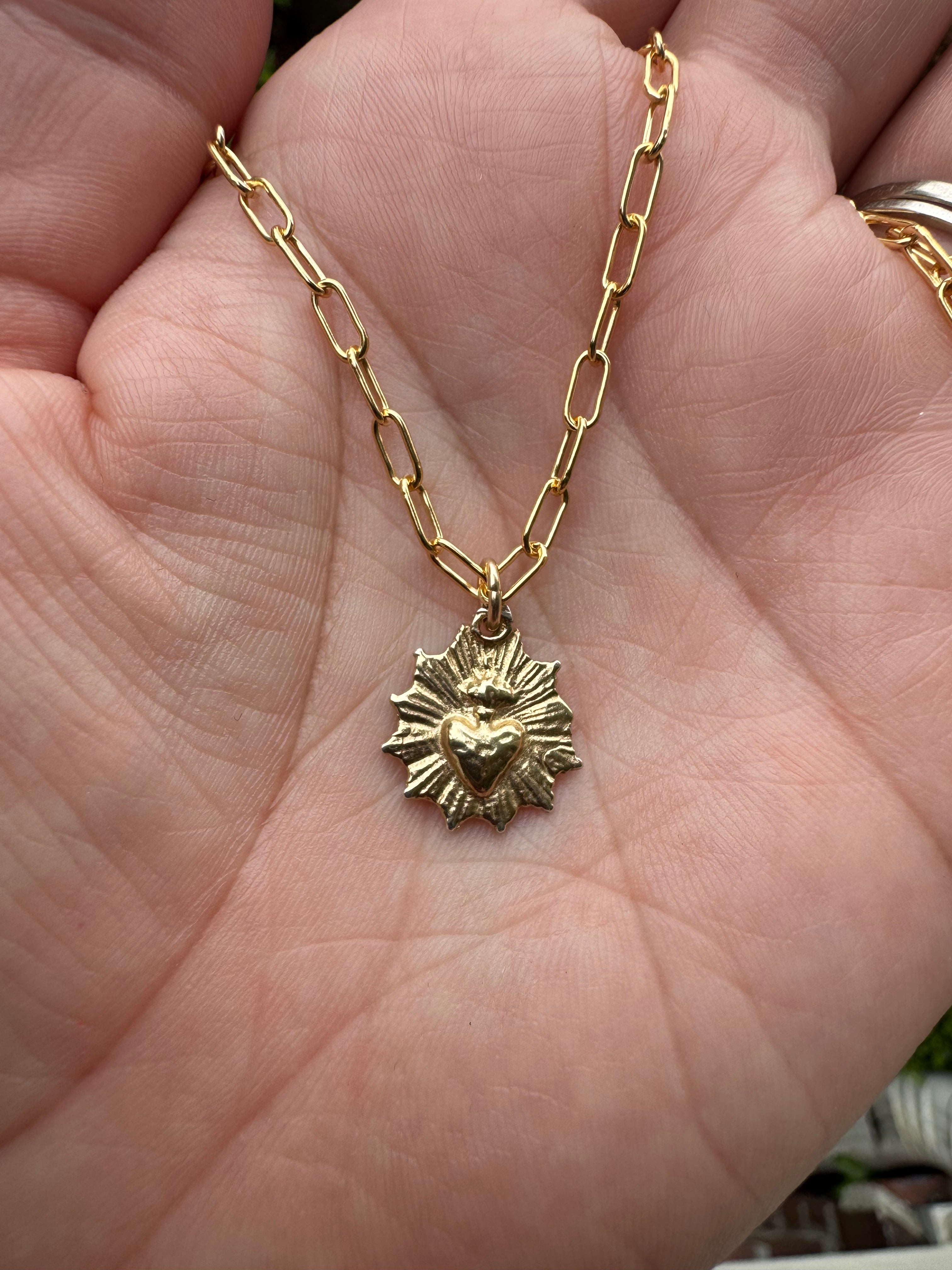 Scalloped necklace with gold sunburst pendant held in hand, small-link chain visible
