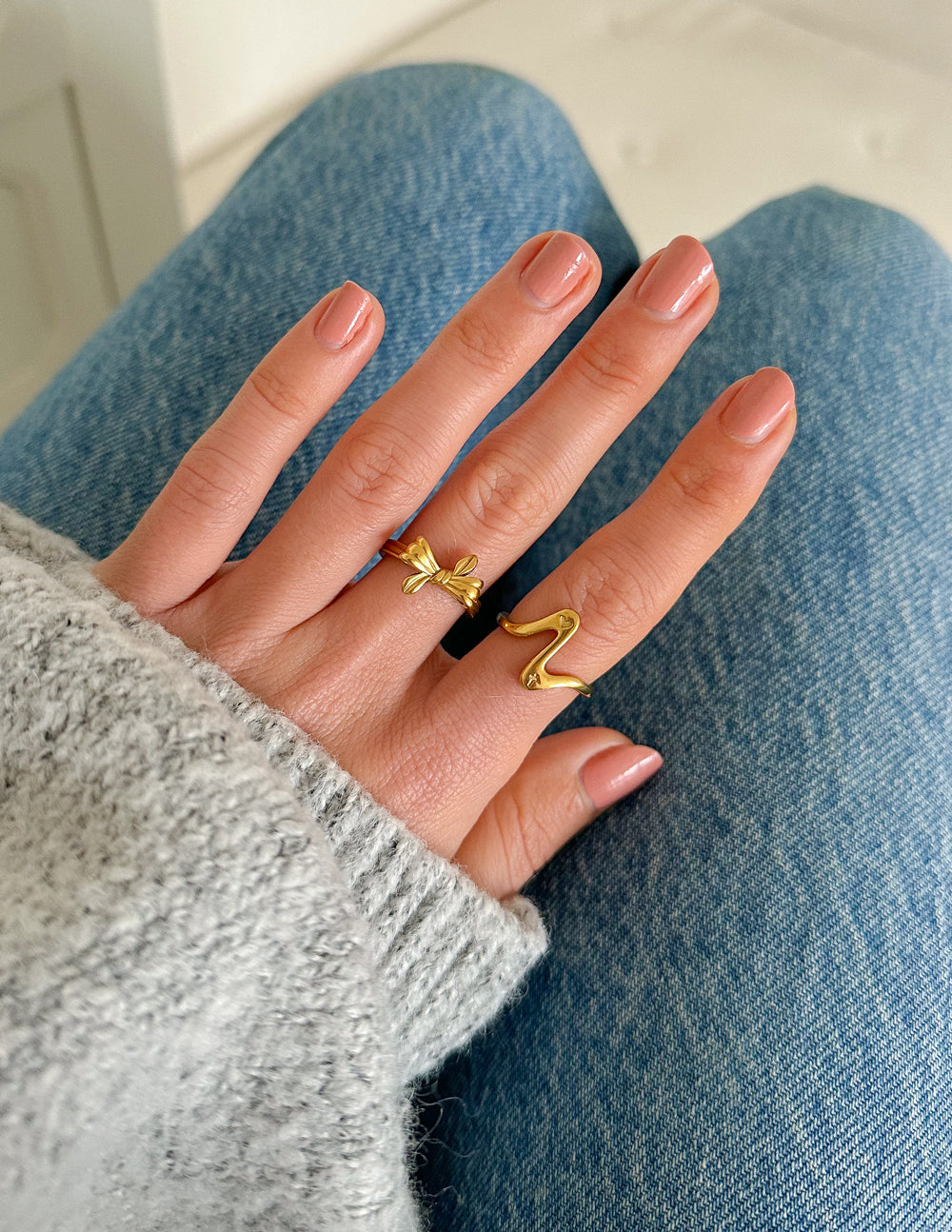 Gold wavy heart ring on hand with glossy nails, open heart motif