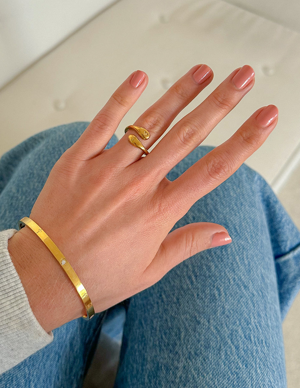 Gold-tone cuff bracelet on wrist with small gemstone-studded panel and side posts