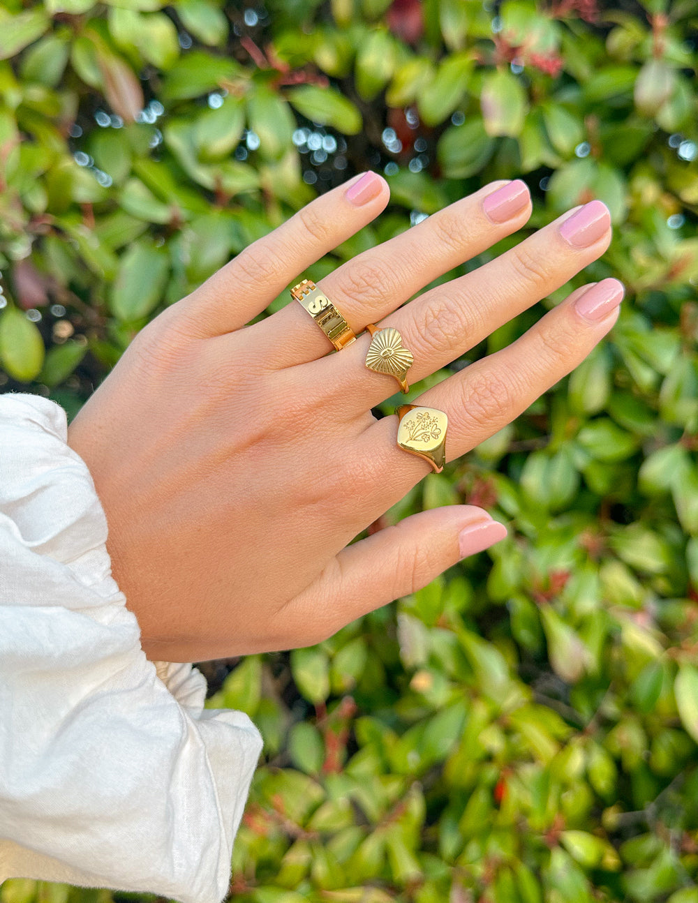 Gold-tone floral signet ring on finger with engraved floral crest