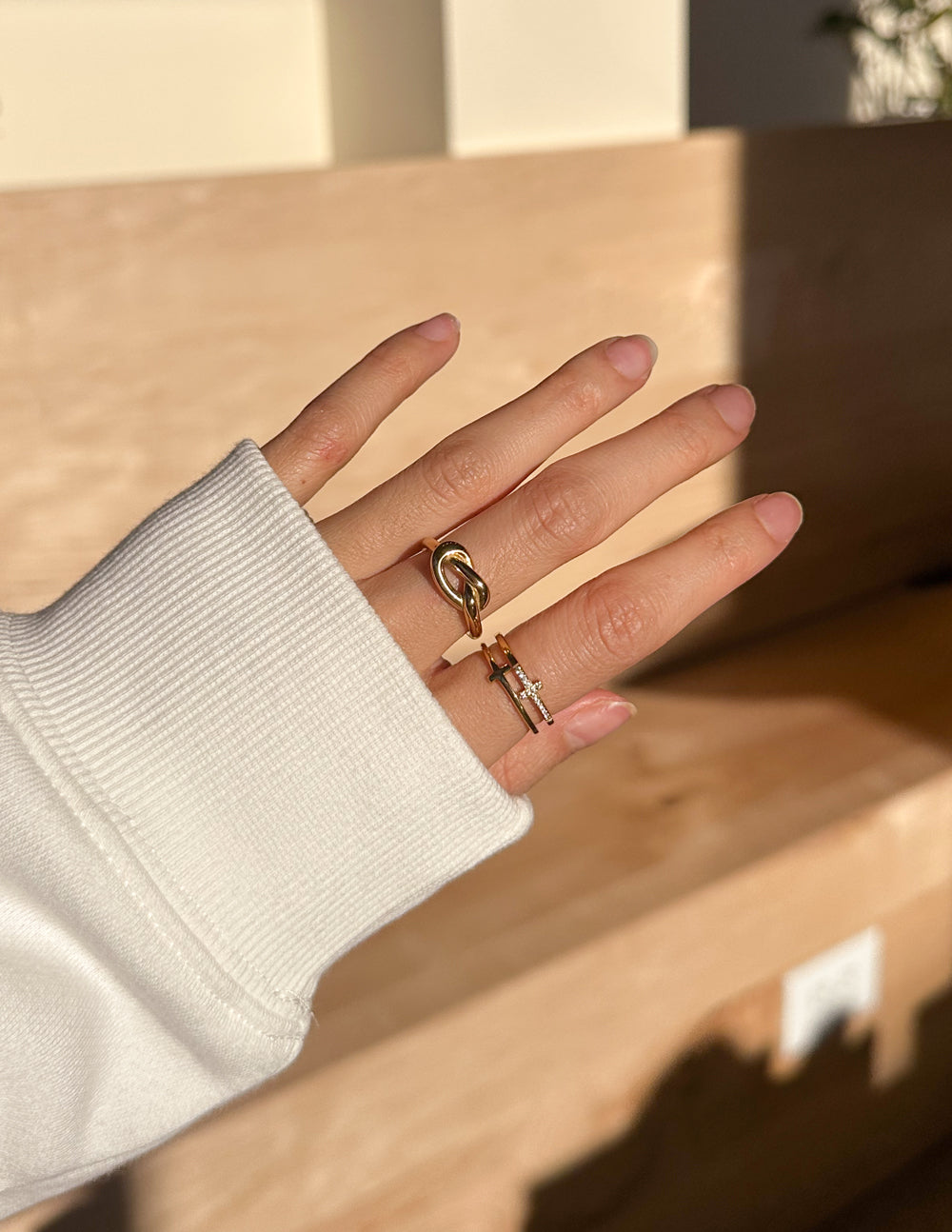 Gold knot ring on finger, stacked with a cross-accent band