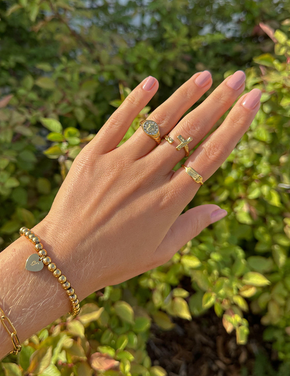 Gold tone signet ring and stacked bands on hand, engraved details