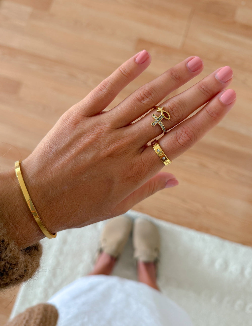 Gold-tone gemstone logo ring with cross motif and engraved band on finger