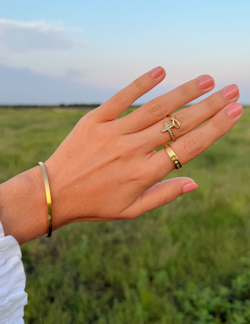 Gold-tone gemstone logo ring with cross motif and small stones on finger