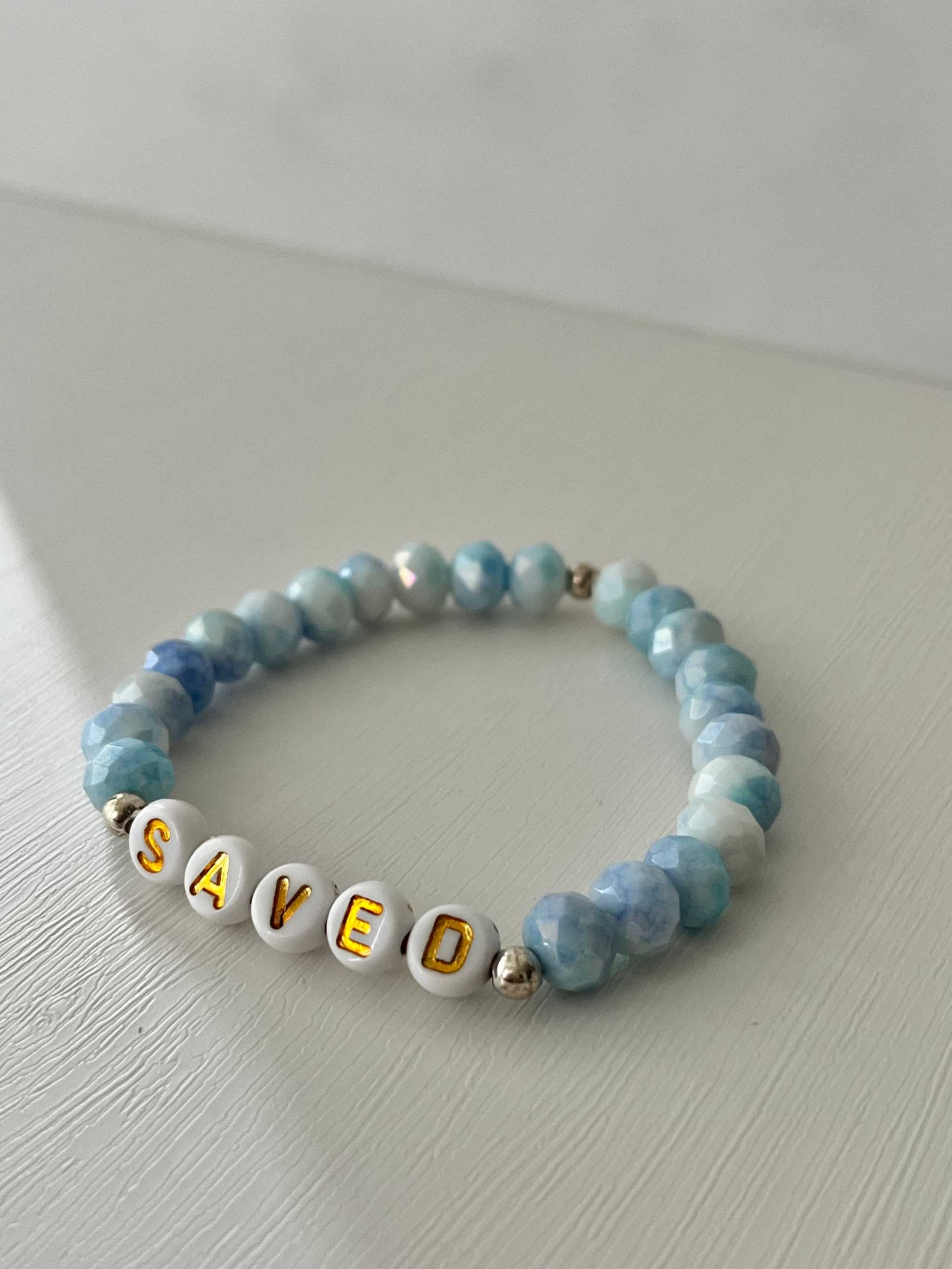 Light blue beaded bracelet with gold-accented 'SAVED' letter beads