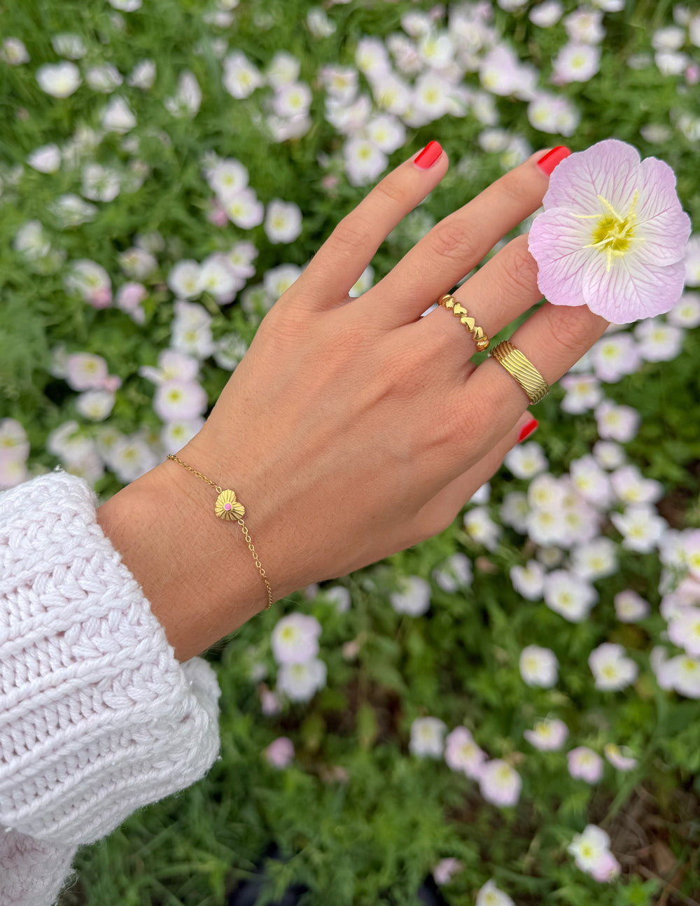 Gold link bracelet on wrist with pink heart charm; adjustable chain
