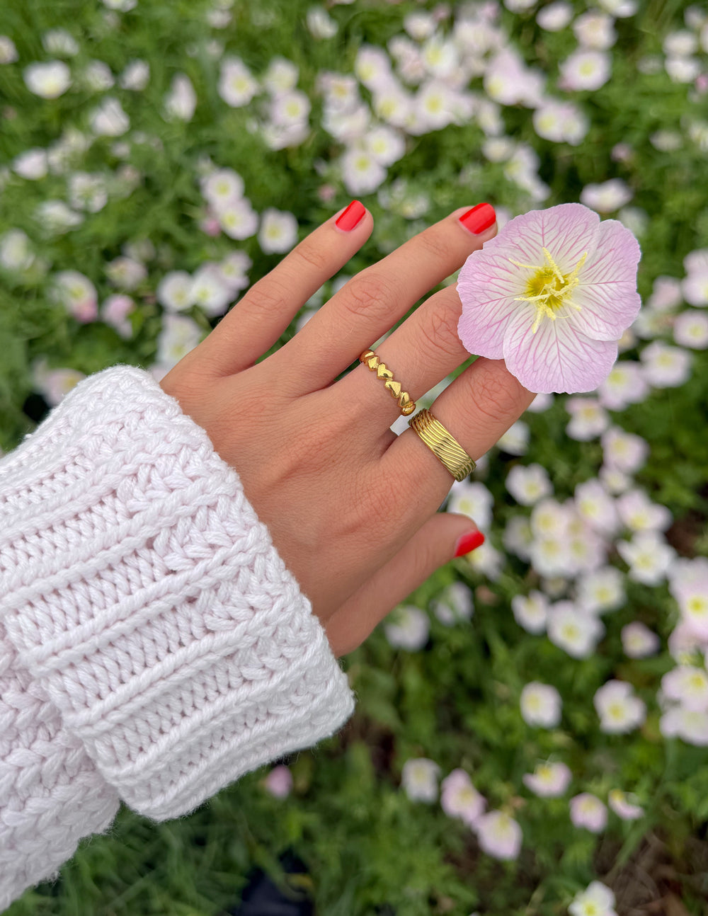 Gold band ring with infinity heart links, worn with red nails