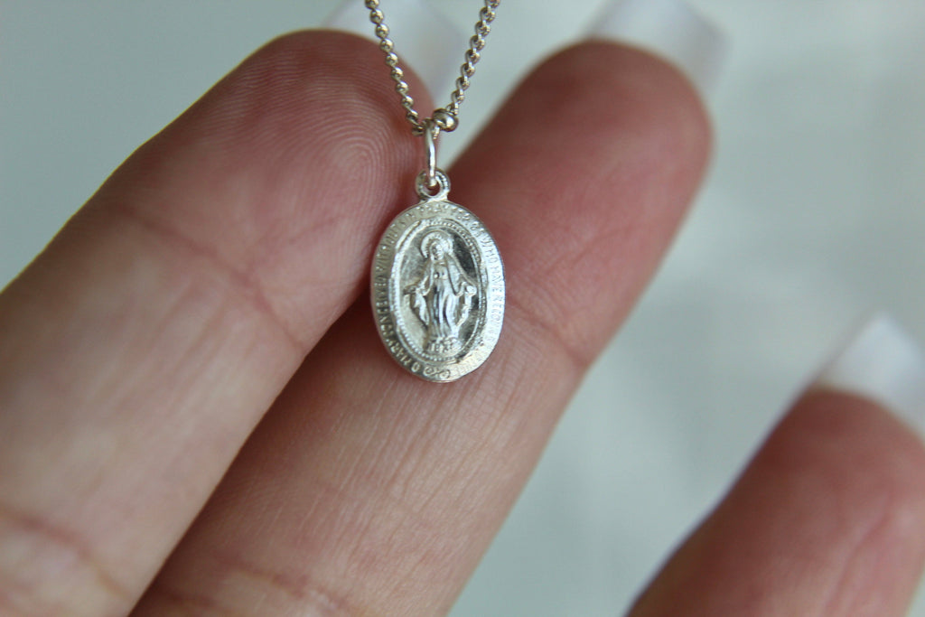 Silver miraculous medal necklace featuring an oval pendant with praying figure