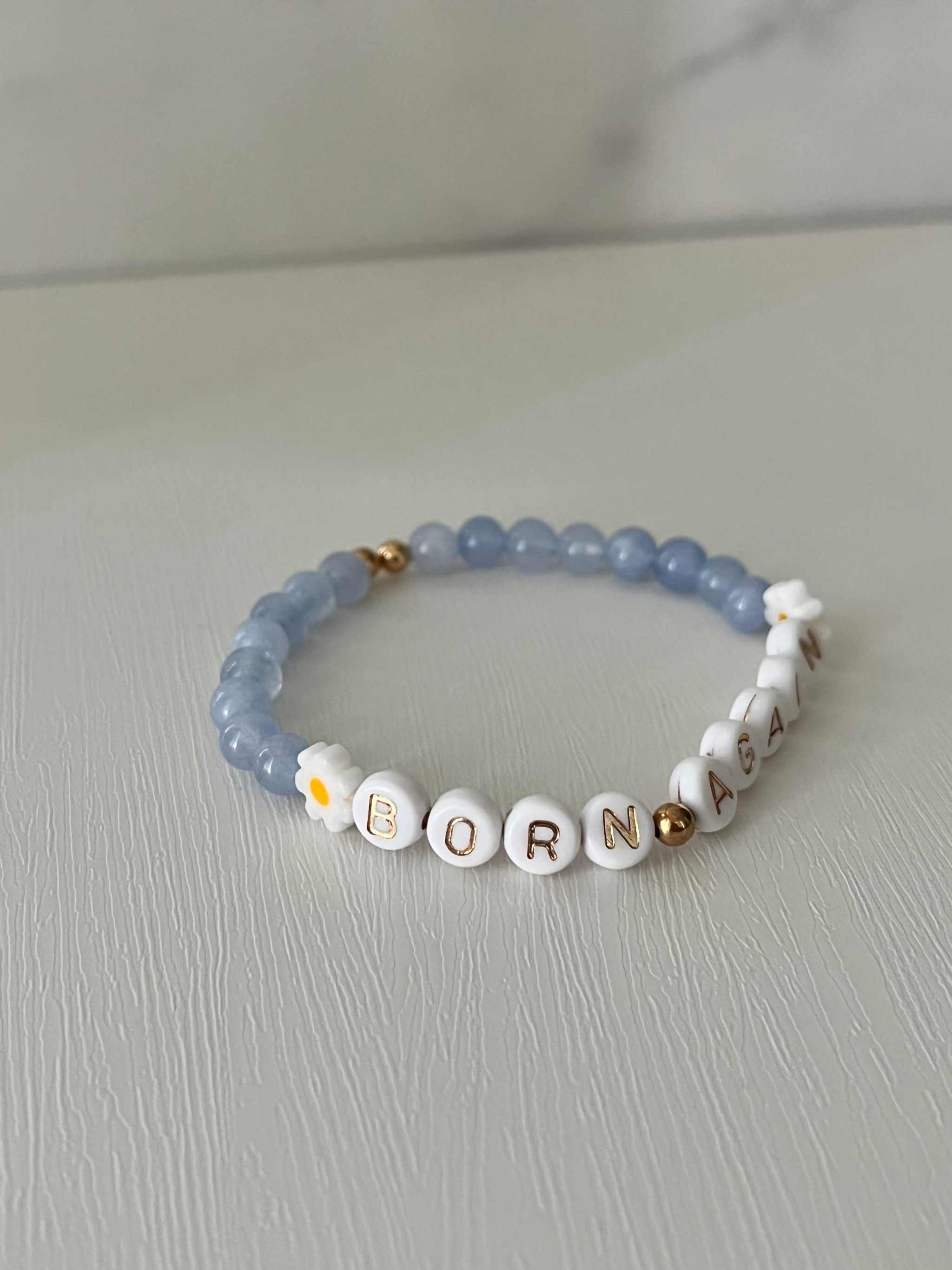 Sky blue bracelet with white letter beads spelling “BORN AGAIN” and tiny flower charms.
