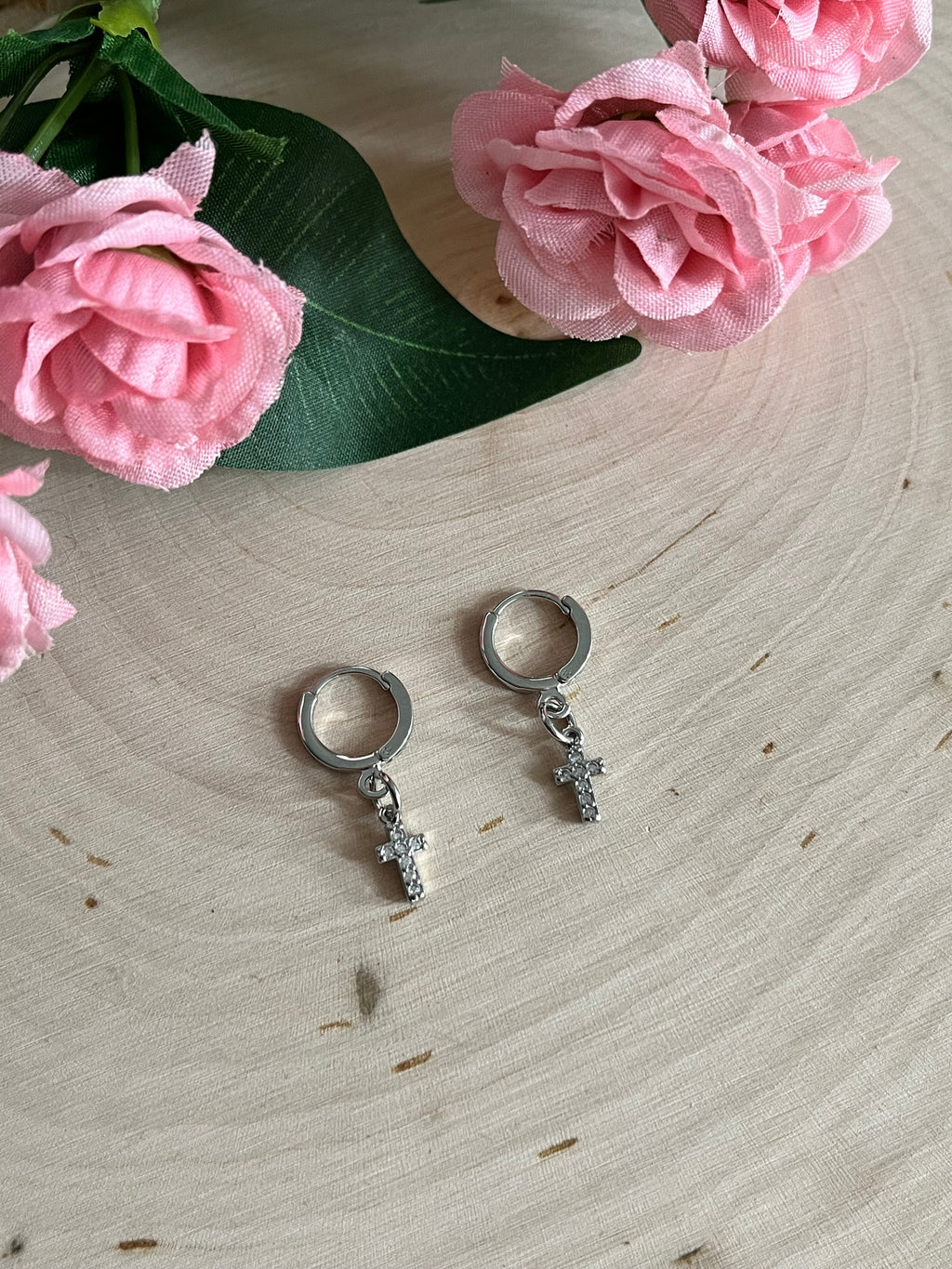 Silver huggie hoop earrings with cross charms, shown on light wooden surface