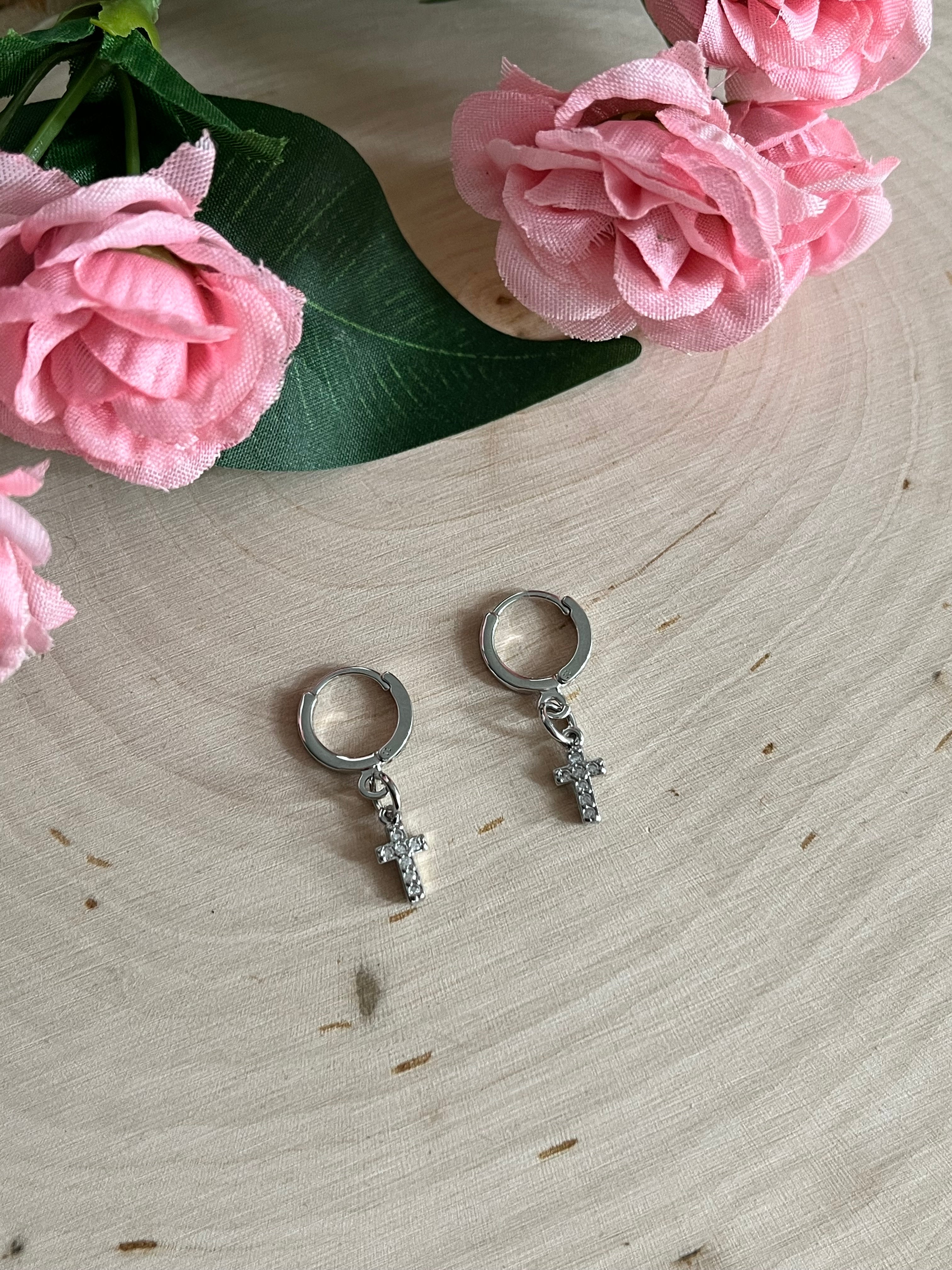Silver huggie hoop earrings with cross charms, shown on light wooden surface