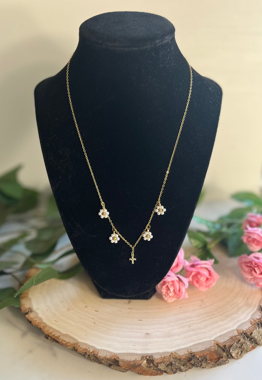 Gold cross pendant necklace with white daisy charms on a display bust