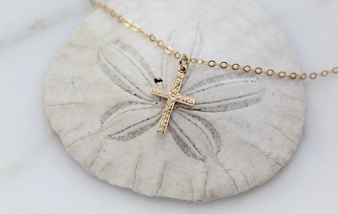 Gold cross pendant necklace with chain draped on seashell, engraved cross