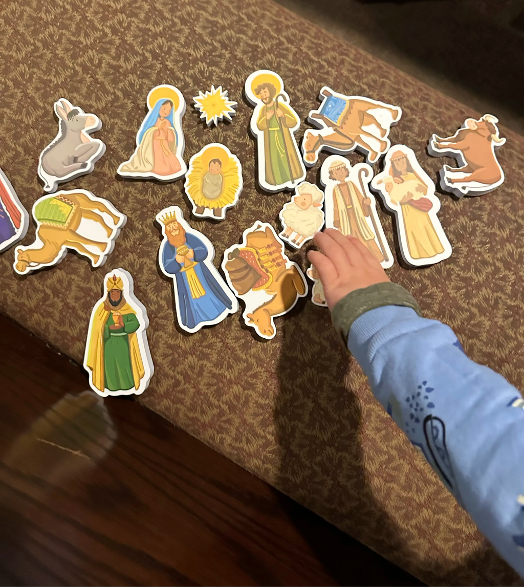 Child hand selecting nativity bath toy cutouts on a fabric-like surface