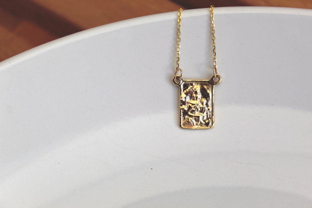 14K gold scapular pendant necklace with square charm over a white dish background