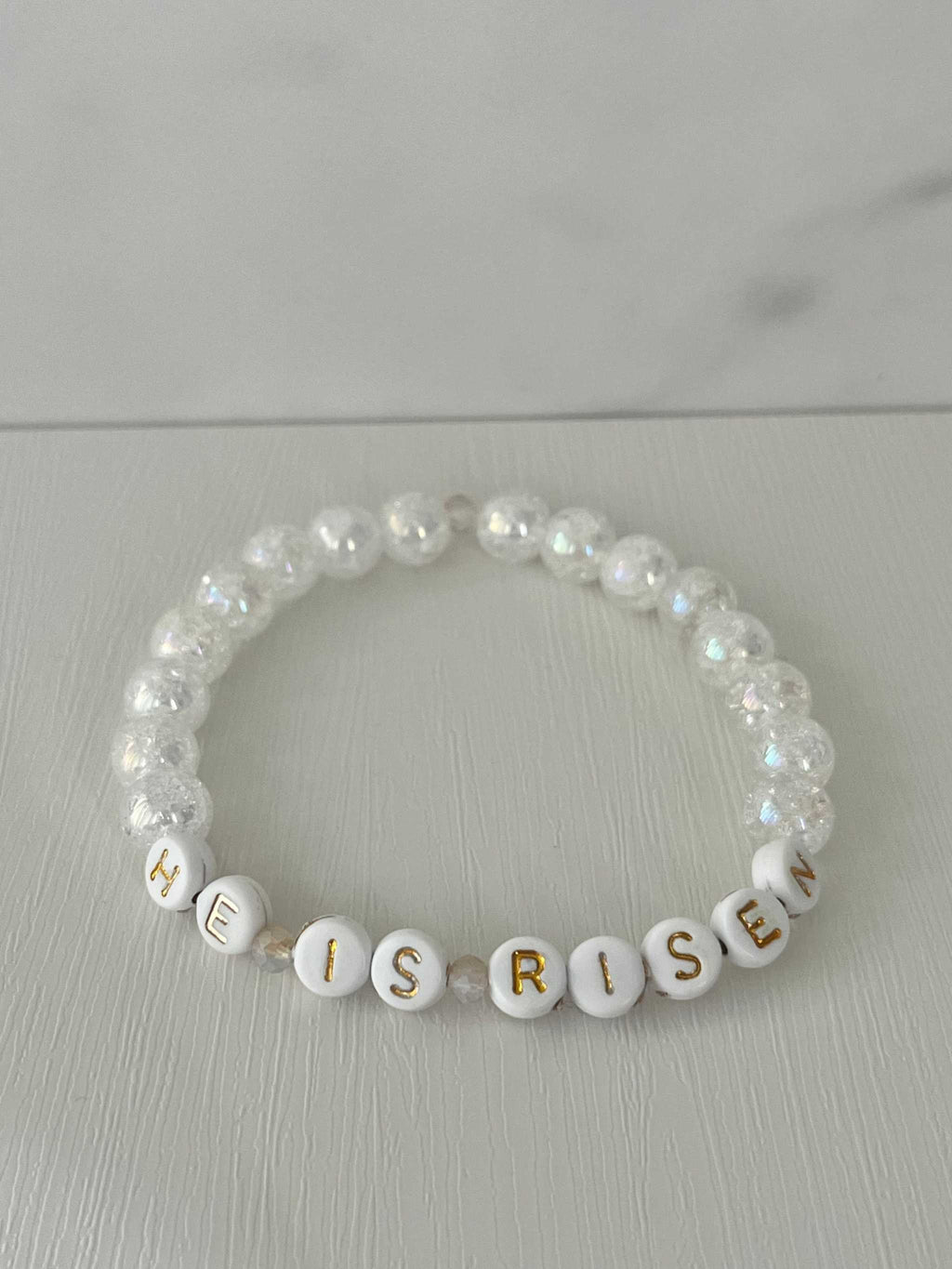 White pearl bead bracelet spelling “HE IS RISEN” with gold cross charm