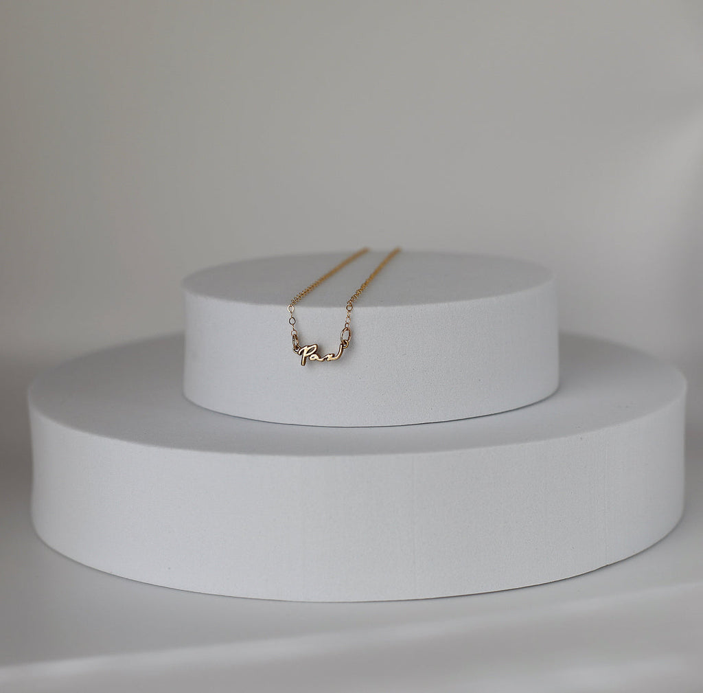 Gold Pax pendant necklace resting on white display pedestal