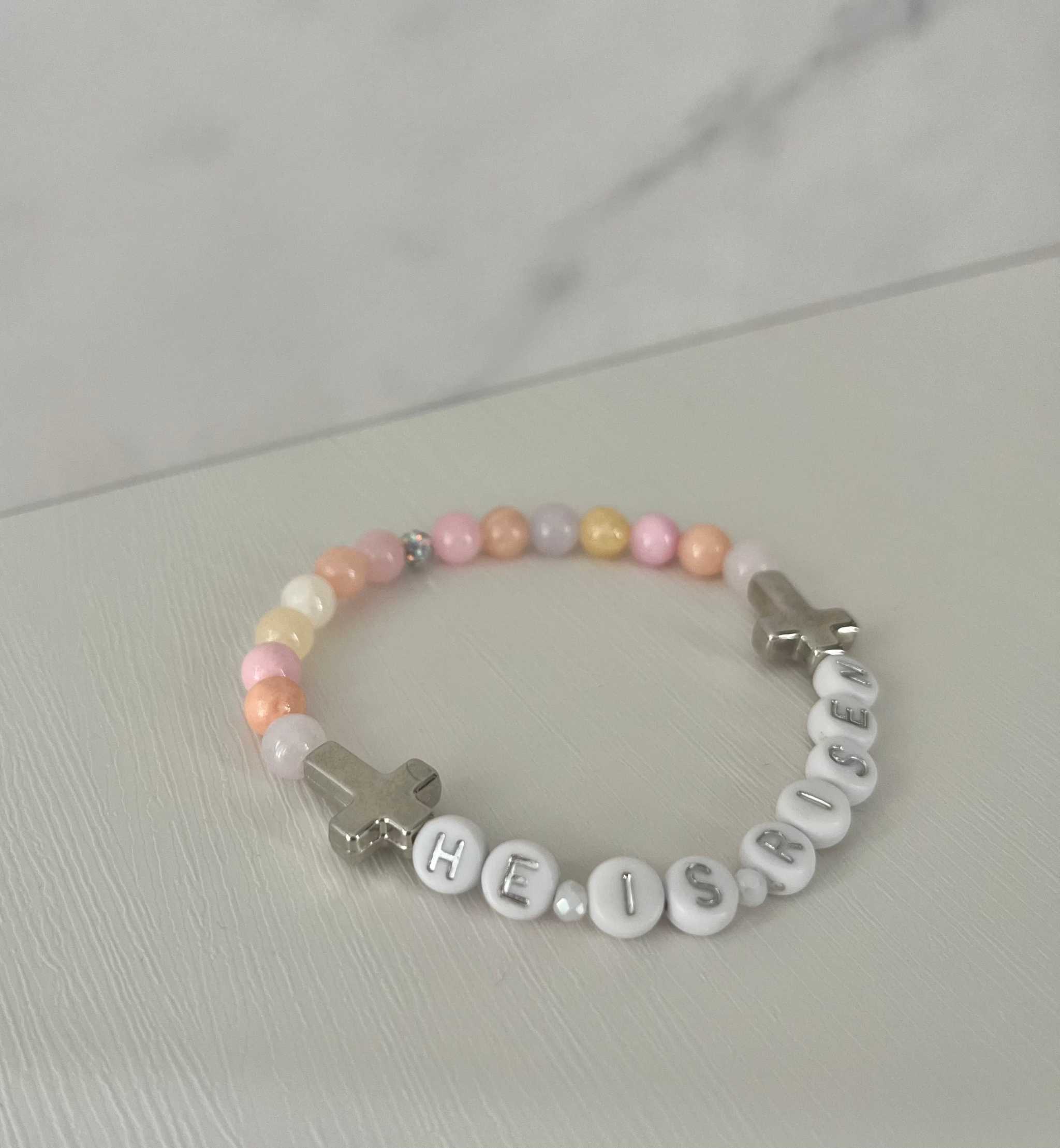 Pastel pink bead bracelet with 'HE IS RISEN' letter beads and silver cross charm
