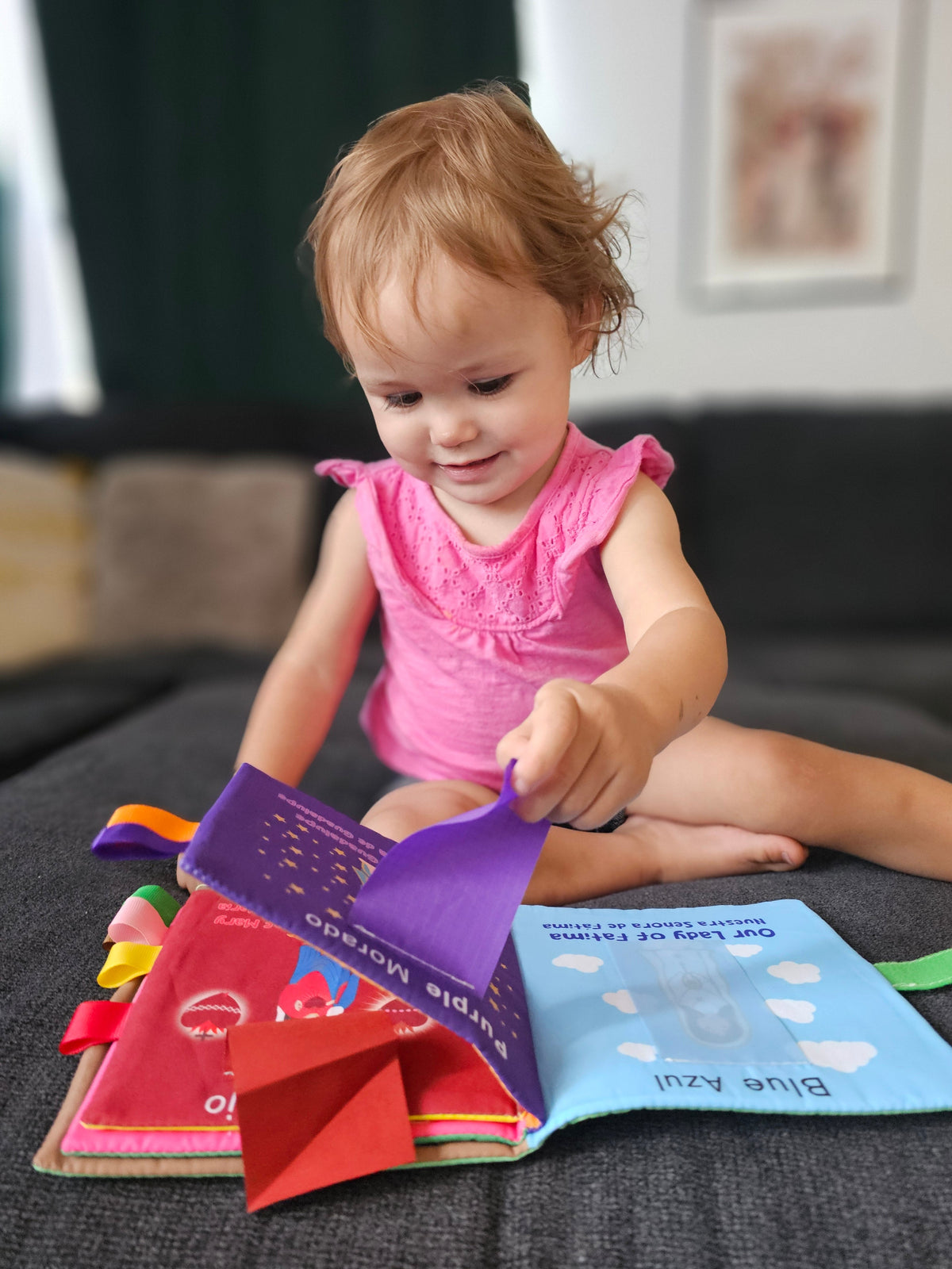 Toddler touching an open purple and red fabric Mary colors book.