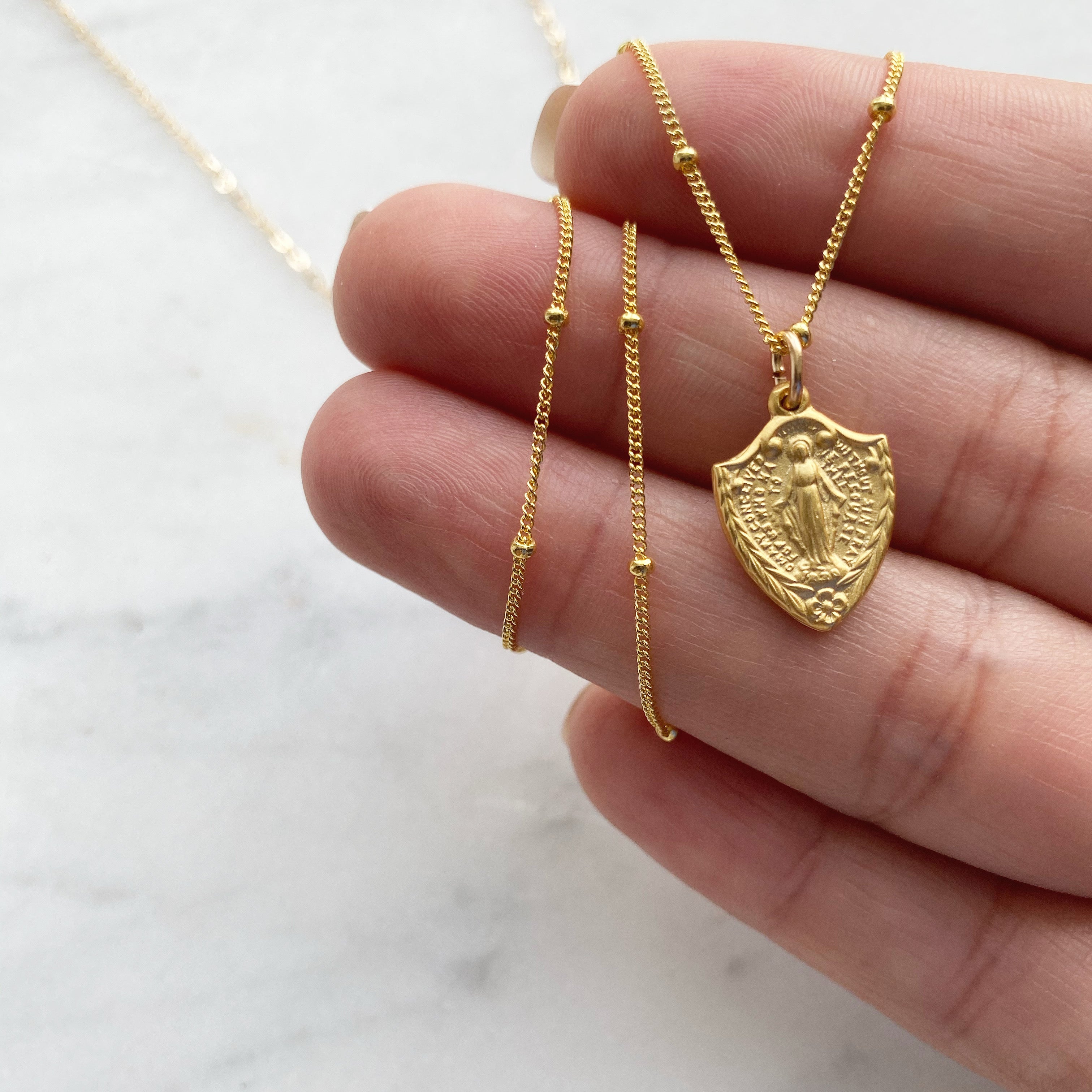 Gold-tone shield pendant necklace with religious figure, thin chain design