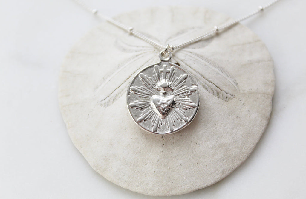 Silver round sacred heart coin pendant necklace on chain with a radiating design.