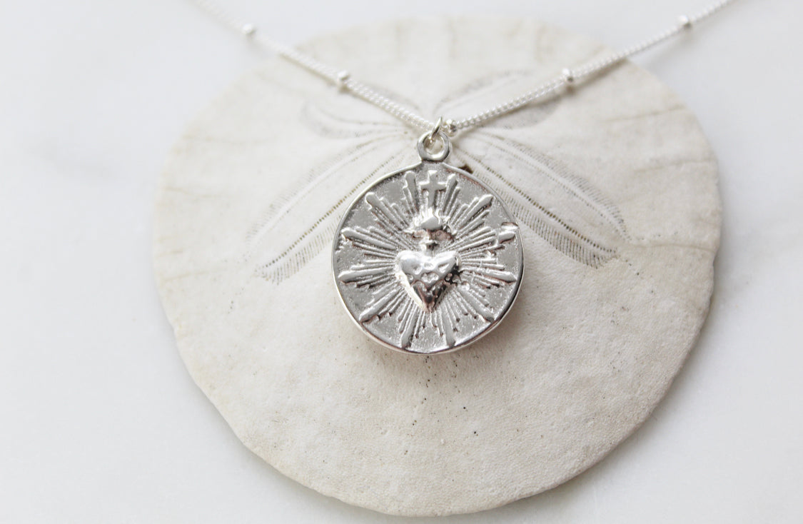 Silver round sacred heart coin pendant necklace on chain with a radiating design.