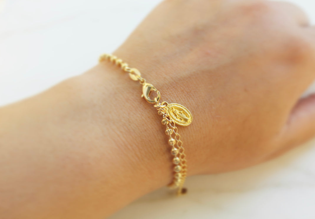Gold-tone medal bracelet on wrist with oval charm and small link chain.