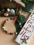 Beaded bracelet with red, green, and white beads and a small silver cross charm