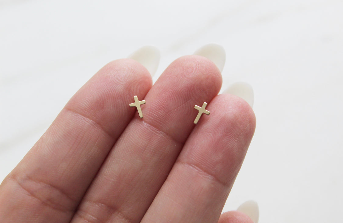 Two 14k gold cross stud earrings resting on palm, small cross icons