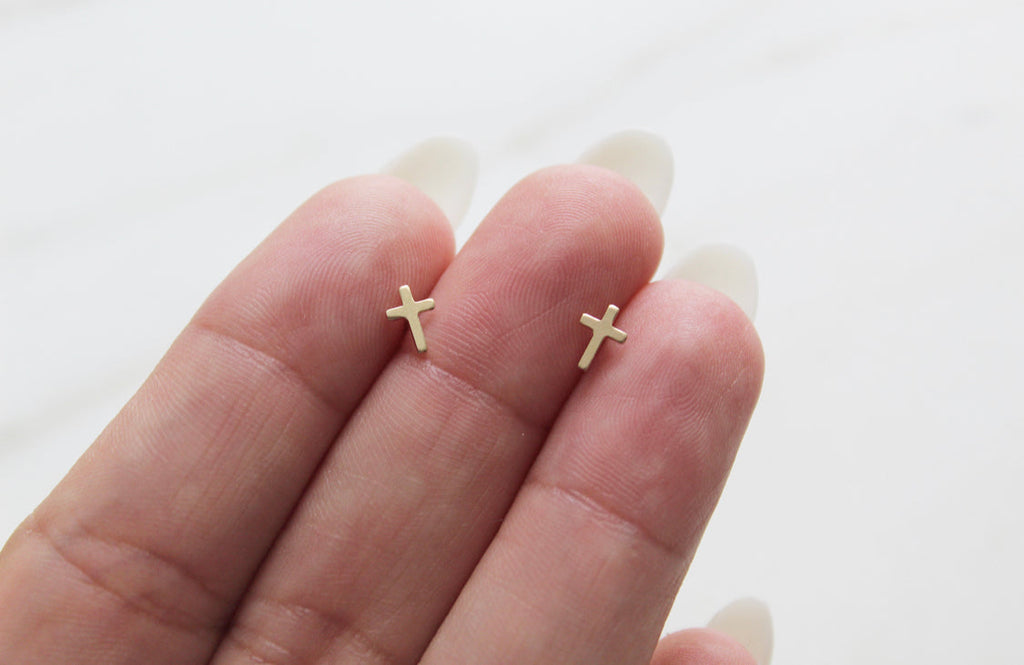Pair of gold-tone cross stud earrings on an open palm, close-up.