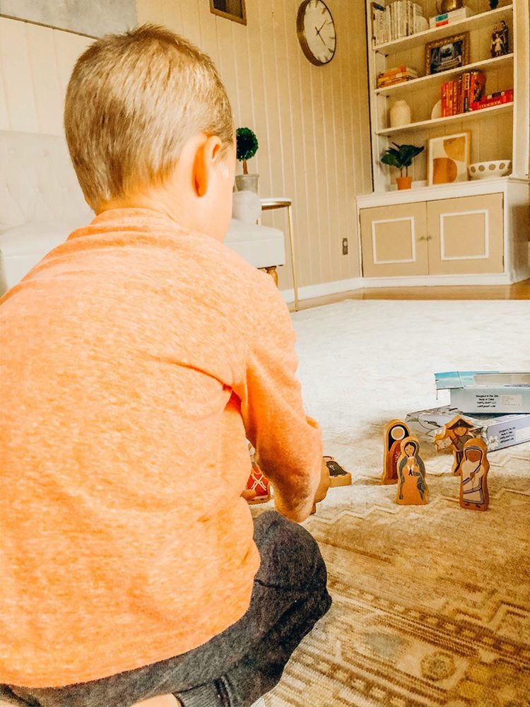 Religious wooden peg figures on floor near a child, small standing characters
