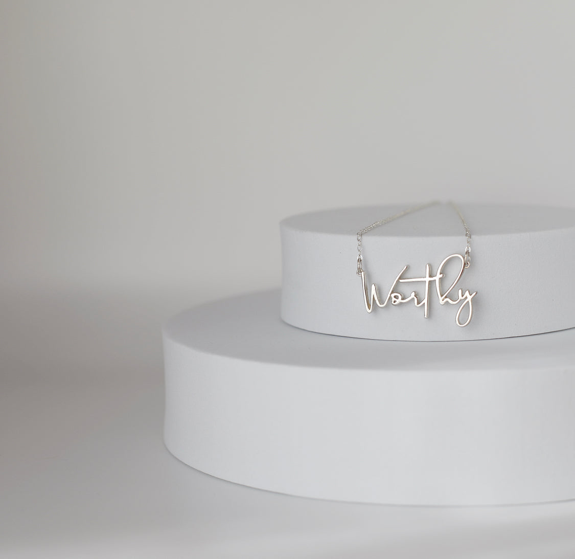 Sterling silver Worthy pendant necklace on a pedestal stand