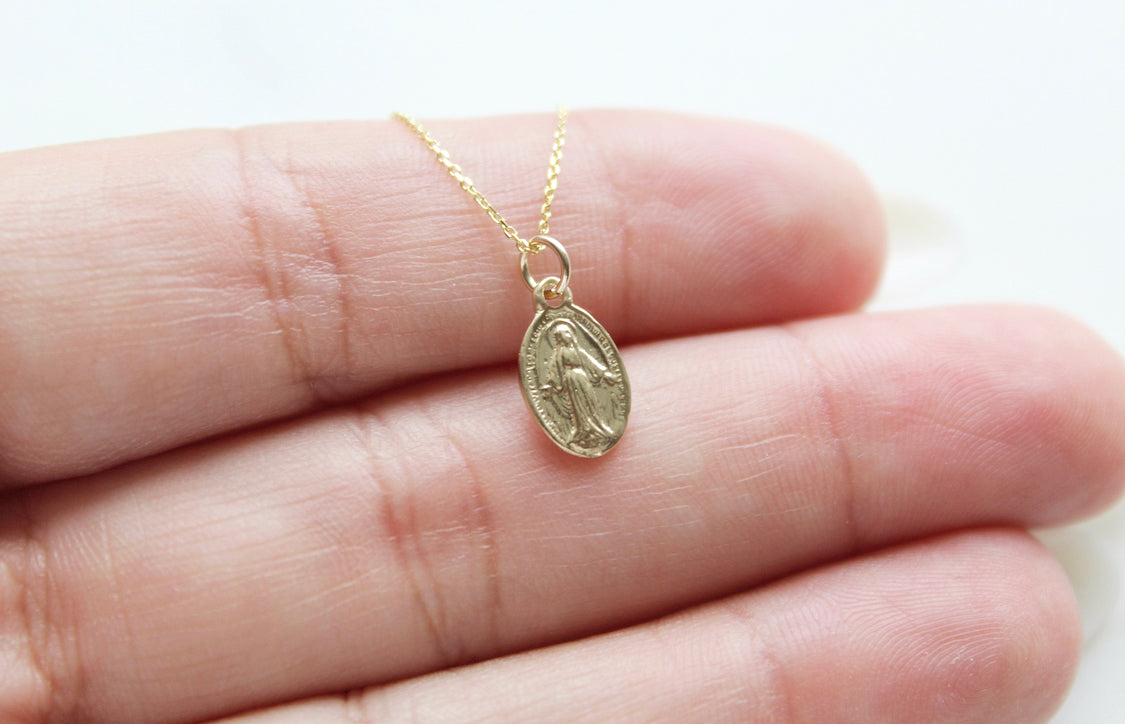 14k gold miraculous medal necklace pendant held in hand, chain visible