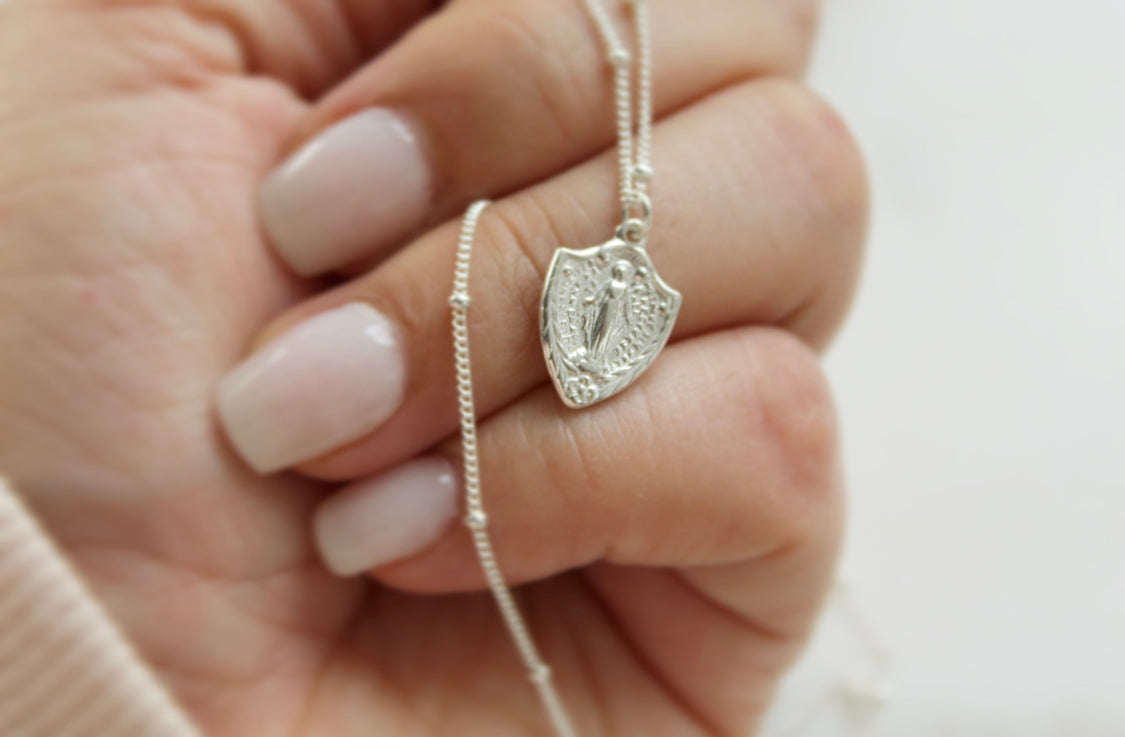 Sterling silver shield pendant necklace with Virgin Mary figure on cable chain, held