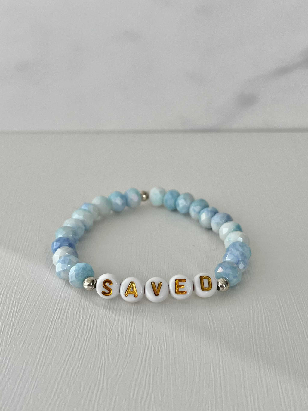 Light blue beaded bracelet with 'SAVED' letter beads and small gold spacers