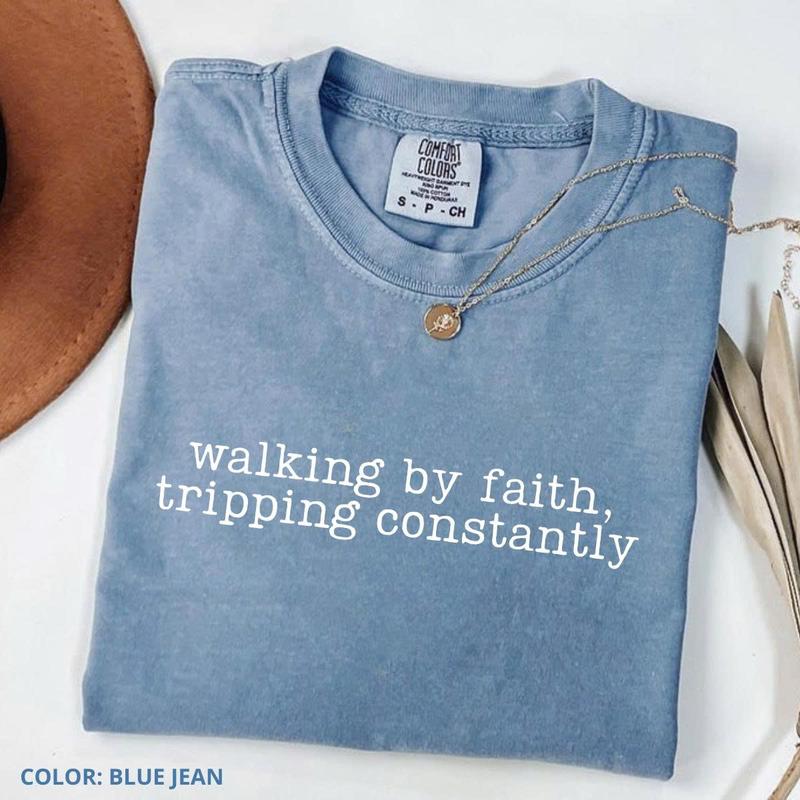 Women’s crewneck graphic tee, medium blue with “walking by faith, tripping constantly”