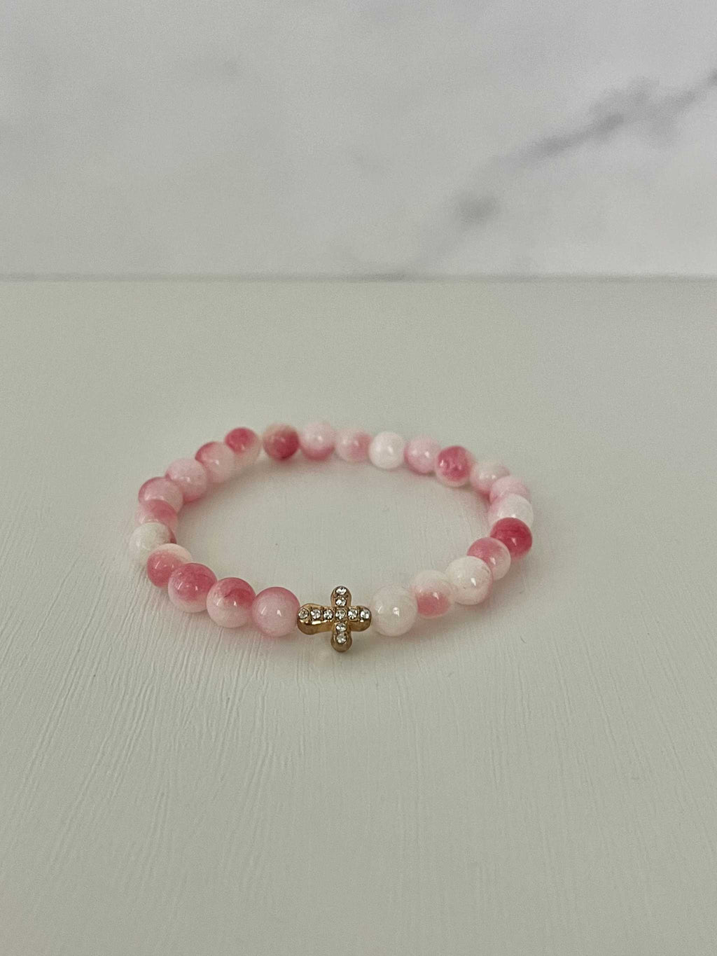 Pink beaded cross bracelet with gold cross charm and stretchy elastic band.