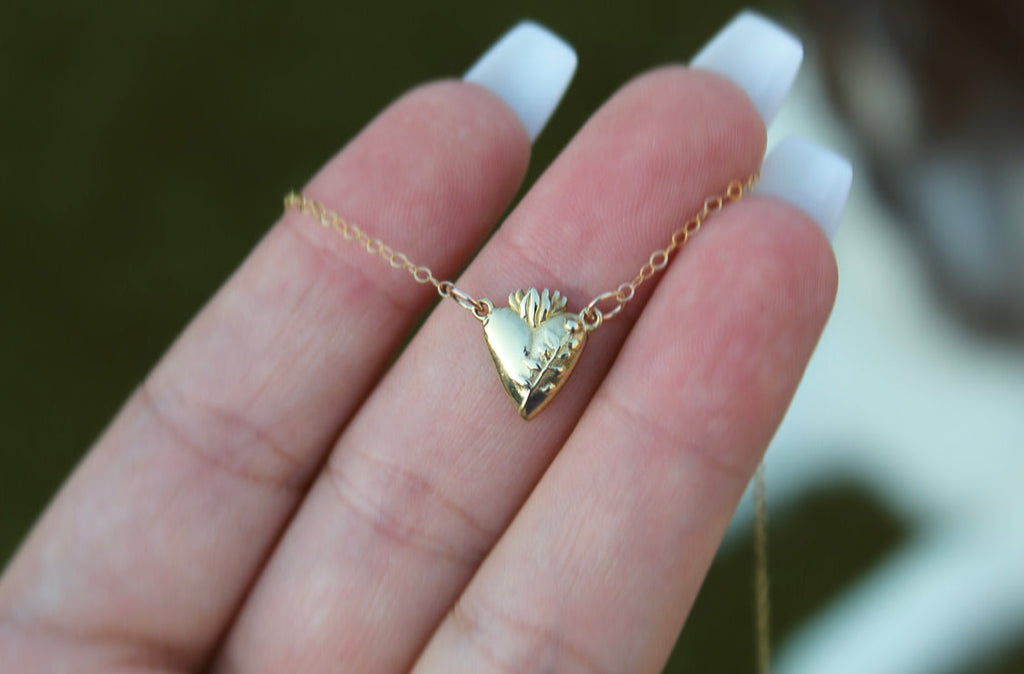 Gold heart pendant necklace in hand, chain with flower-like detail