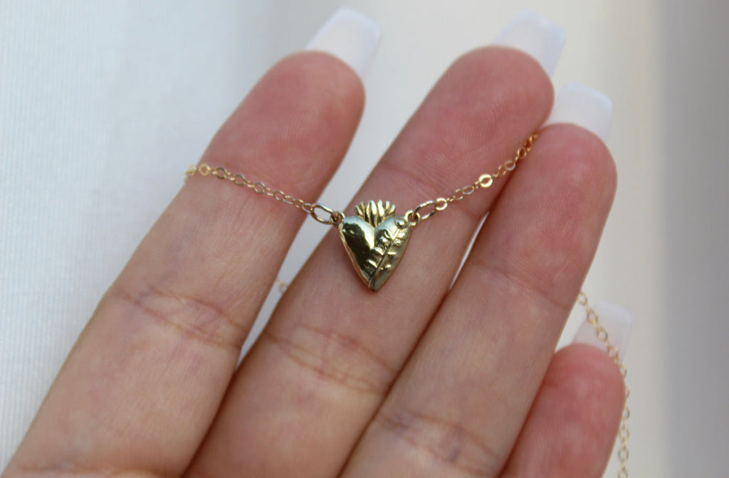 Gold heart pendant necklace with chain detail held in palm