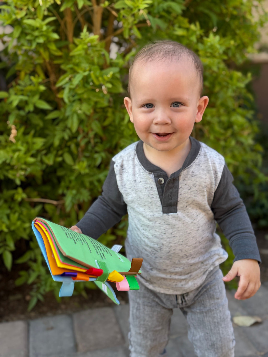 Baby holding an illustrated fabric Mary colors book with multicolor page edges.